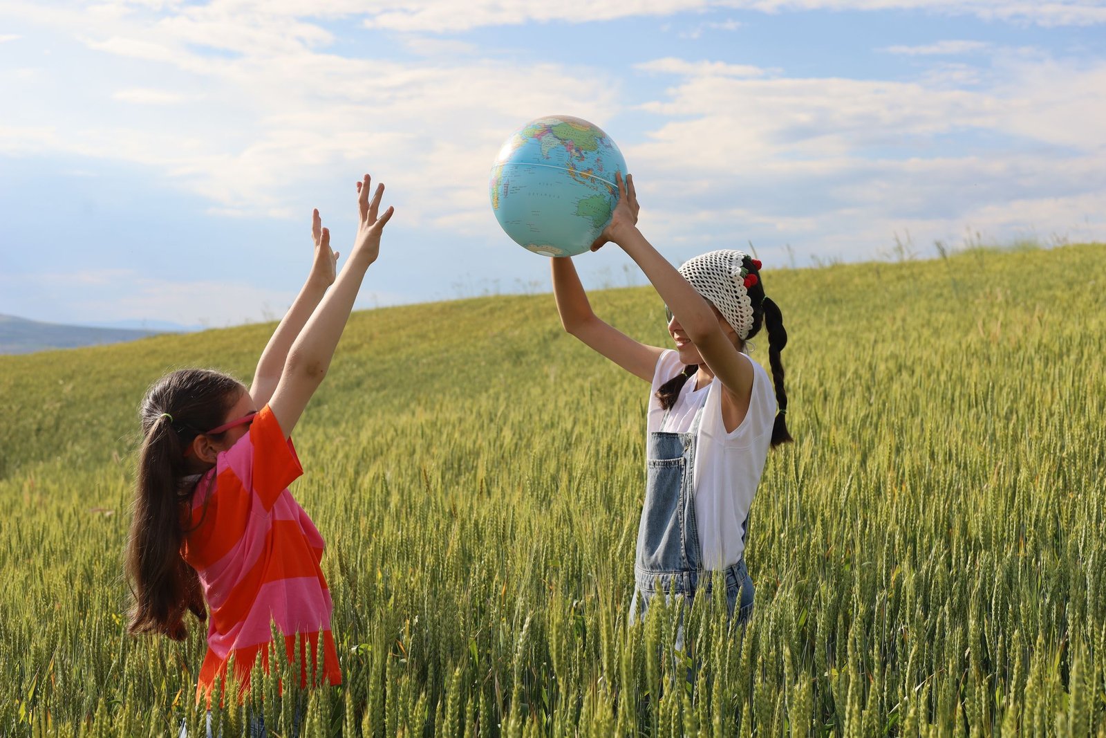 Joyful kids holding an earth globe in a lush wheat field, symbolizing global unity.