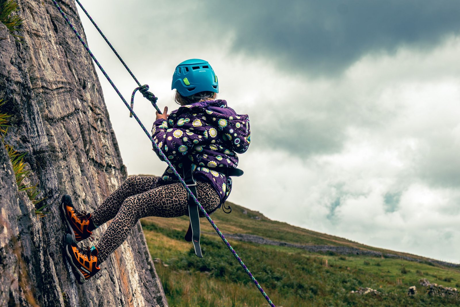 Young girl rock climbing on a cloudy day in the English countryside, showcasing adventurous spirit and safety gear.