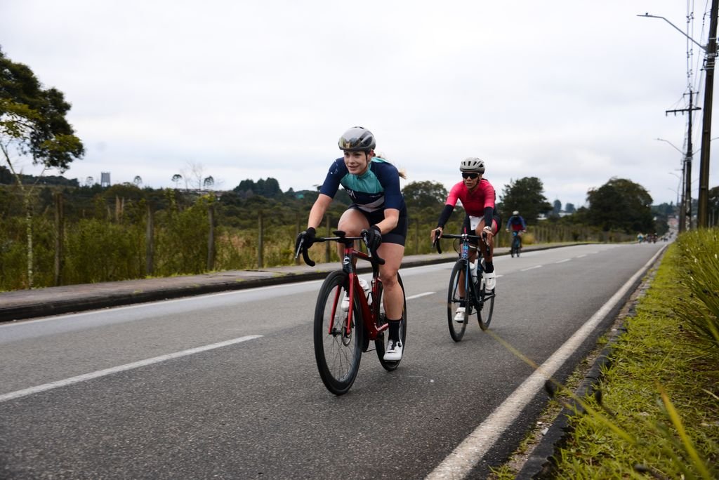 Athletic cyclists in vibrant gear racing on an open road in Quatro Barras, Brazil.