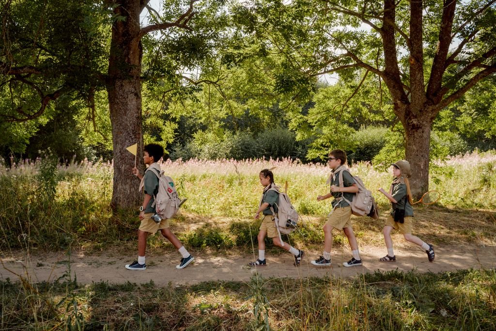 Group of young scouts trekking through a sunny forest trail with backpacks and uniforms.