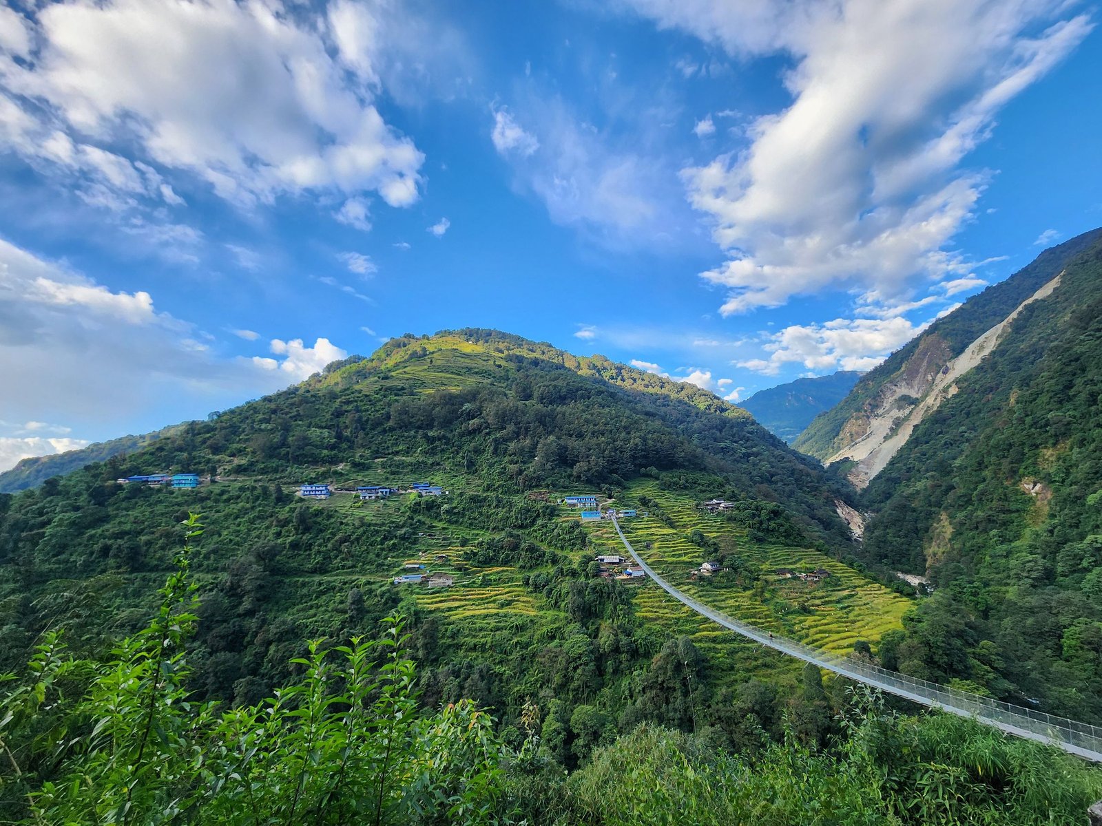 Stunning view of lush mountains and a suspension bridge in Nepal under a clear blue sky.